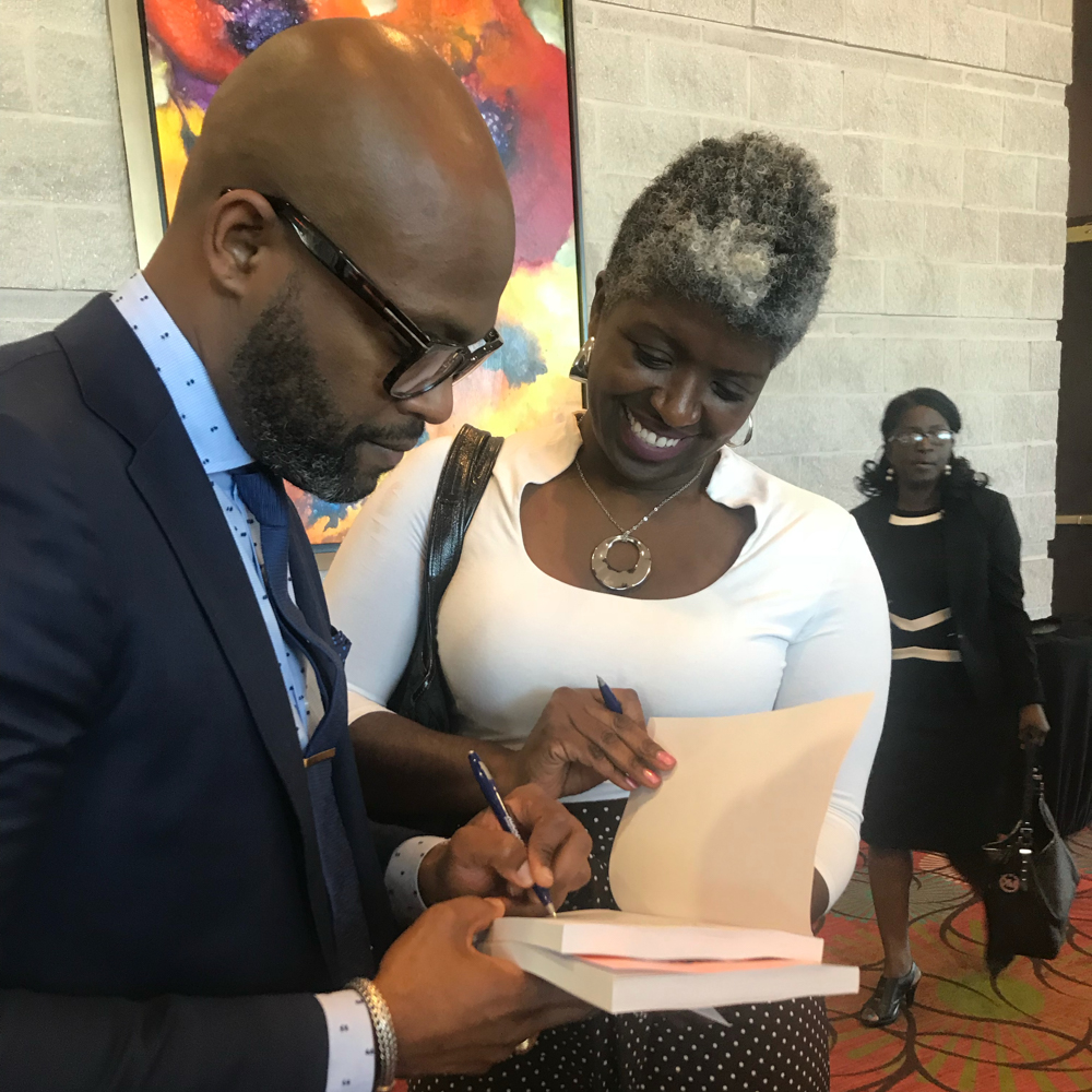 Dr. Dickey signing an autograph on a book with a woman on white blouse