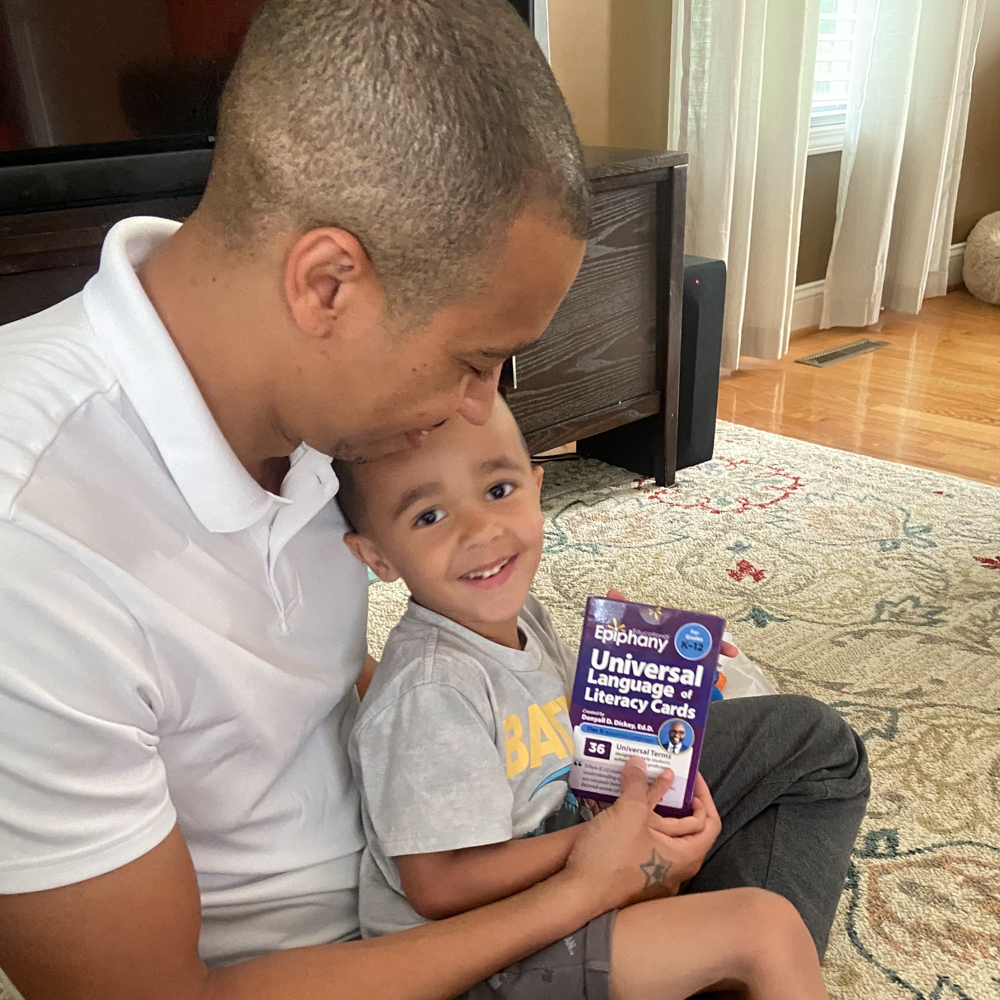 A dad and a kid holding a box of universal language of literacy cards