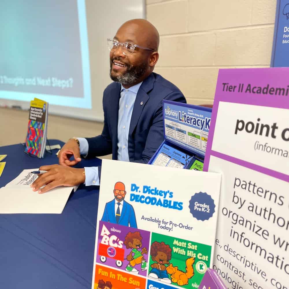 Dr. Dickey smiling while holding a pen and a book with learning materials beside him