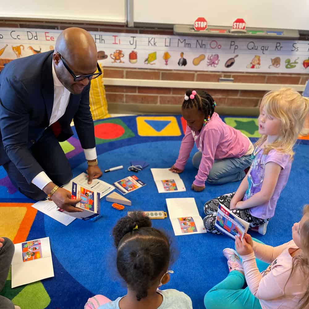 Dr. Dickey with a group of preschool students kneeling on the floor with books